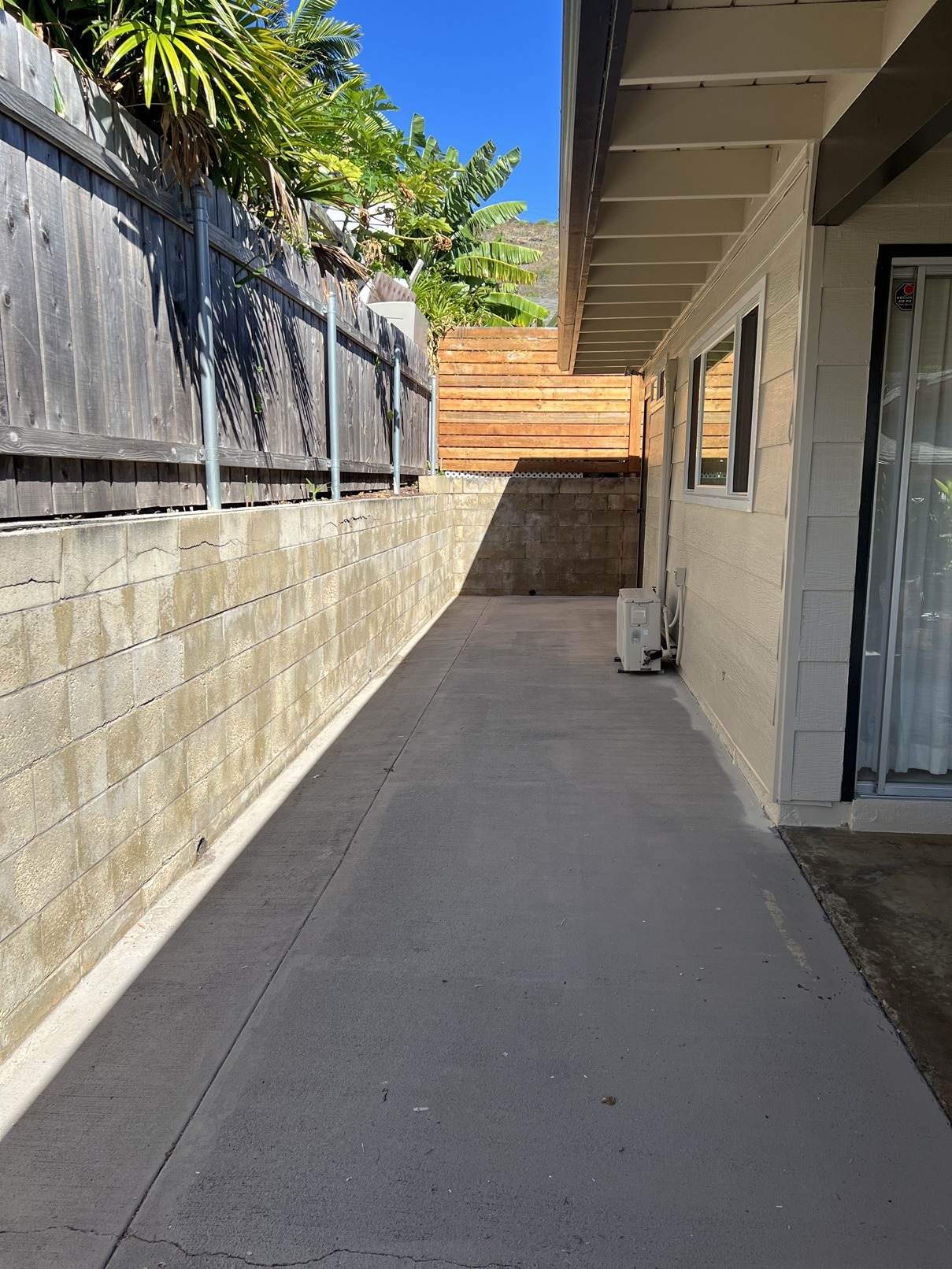 A concrete pathway leads to a house with a wooden fence on the left.